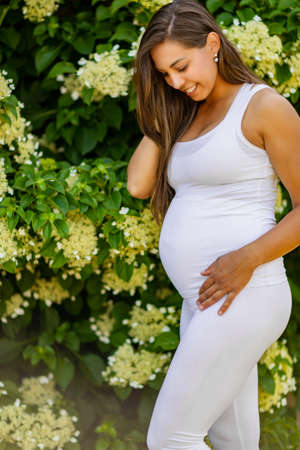 Happy pregnant woman in beautiful garden looking down on bellyの写真素材