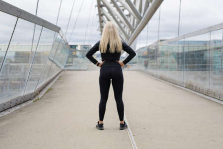 Back of fit blonde woman runner standing on bridge in modern looking cityの写真素材