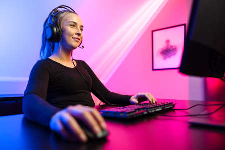 Happy and Beautiful Blonde Gamer Girl Playing Online Video Game on Her Personal Computer.の写真素材