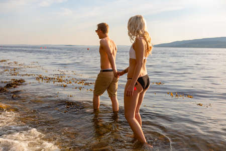 Romantic couple holding hands and walks at the sea shore in the eveningの写真素材
