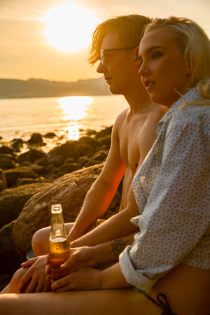 Couple relaxing and drinking beer at the beach at sunsetの写真素材