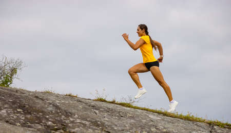 Side view of fitness woman doing high-intensity running on mountainside by the seaの写真素材