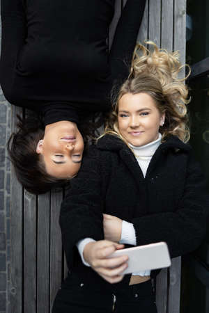 Smiling Friends Lying On Bench Taking Selfie Together in Cityの写真素材