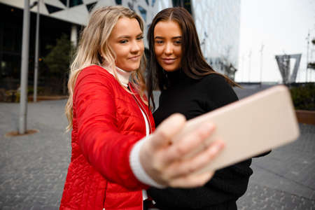 Two Smiling Beautiful Friends Taking Selfie Through Smartphone In Cityの写真素材