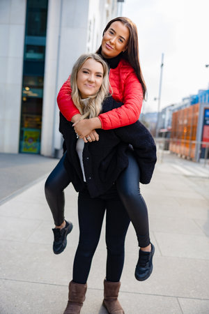 Smiling Female Friends Having Fun and Piggybacking In Cityの写真素材