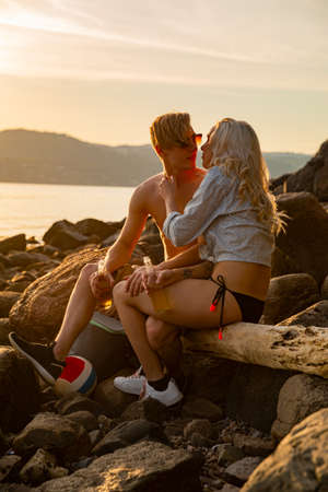 Beautiful Couple Kissing And Drinking Beer While Sitting On Rocksの写真素材