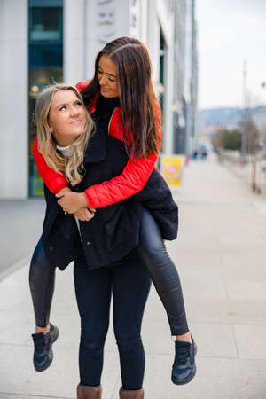 Two Close Woman Friends Having Fun and Piggybacking In Cityの写真素材