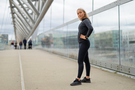 Fit Woman in Black Workout Outfit Standing At Modern Bridge In Cityの写真素材