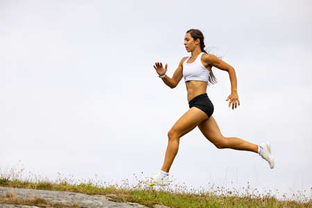Determined Fit Female Athlete Running On Mountain Against Skyの写真素材