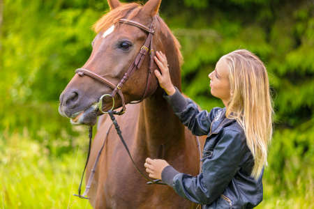 Young woman patting her arabian horse standing in the fieldの写真素材