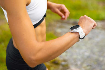 Close-up of athletic woman using fitness smart watch device under workoutの写真素材
