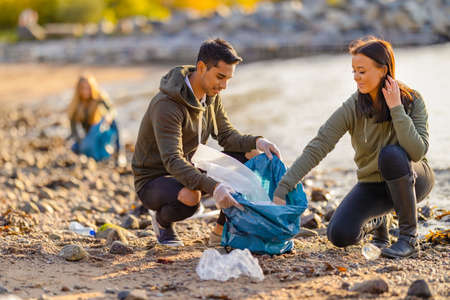 Team of dedicated and smiling volunteers collecting plastic garbage at beachの写真素材
