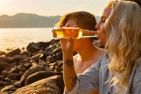 Young Woman Drinking Beer By Boyfriend At Beachの写真素材