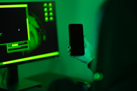 Cyber security concept showing hacker holding mobile phone in dark roomの写真素材