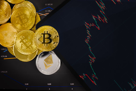 Golden bitcoin and crypto coins by digital tablet over chartの写真素材