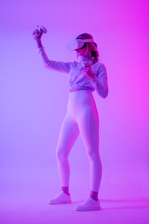 Woman immersed in virtual reality with headset and controllers in neon lightsの写真素材