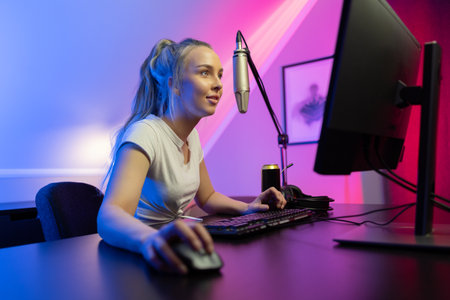 Smiling and focused professional gamer girl with headset play online multiplayer video game on PCの写真素材