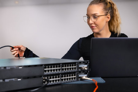IT technician professional configuring network switch and managing network cables and hardware in a data center environmentの写真素材