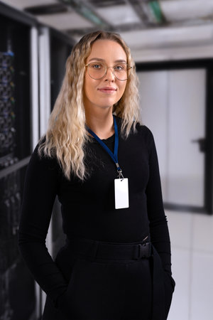 Female IT professional in datacenter with confident expression wearing security identification badge. IT consultant in server and network roomの写真素材
