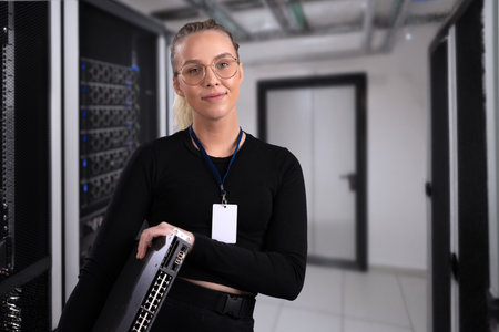 Smiling professional technician holding network equipment in a modern server room setupの写真素材