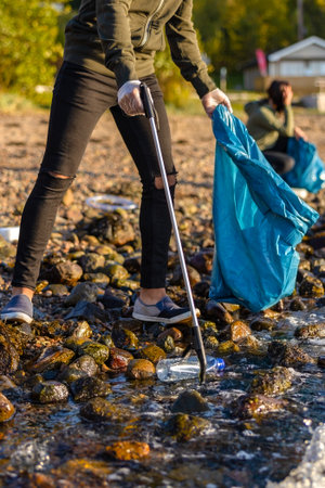 Close-up of volunteer picking up garbage with grabber at beachの写真素材