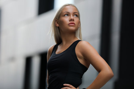 Confident athletic woman posing outdoors in black top, modern city settingの写真素材