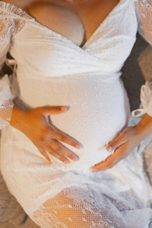 Expectant mother cradling her belly wearing a delicate white lace dress