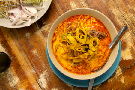 Traditional Thai noodle soup served with fresh garnishes on a rustic wooden tableの写真素材