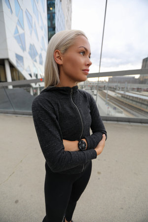 Confident young woman in black activewear standing outdoors near urban buildingsの写真素材