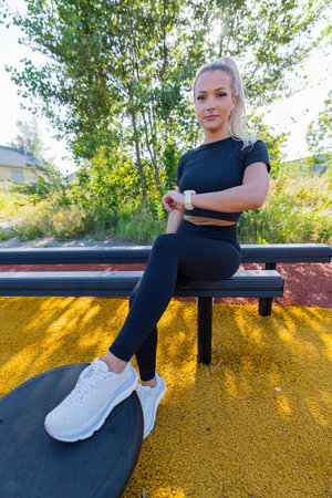 Young woman using smartwatch during outdoor workout on sunny park trailの写真素材