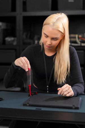 Young woman with blonde hair repairs laptop in a tech workshopの写真素材
