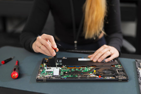 Female IT technician repairing a laptop with screwdriver, open motherboard, performing hardware maintenance and troubleshootingの写真素材