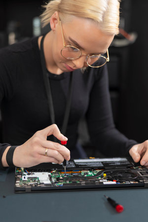 Young female IT technician repairs a laptop with precision and focus in a workshop settingの写真素材