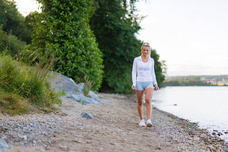 Woman walking on a scenic trail by the lake in outdoor activewearの写真素材