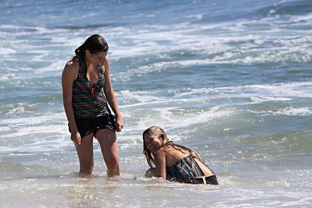 2 young women, playing in the water at the beach.  One is smiling because they both just got hit by a big wave.の写真素材
