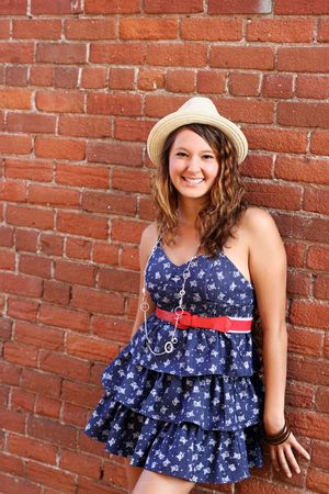 A pretty young girl wearing a blue dress and a hat, leaning against a brick wall.の写真素材