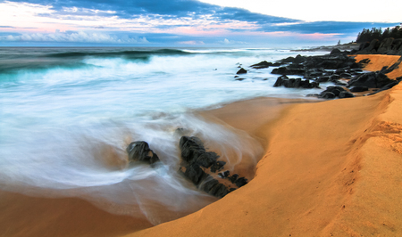 Long exposure of waves crashing on an orange sandy beach at sunset. Tuross Head, New South Wales, Australia.の写真素材