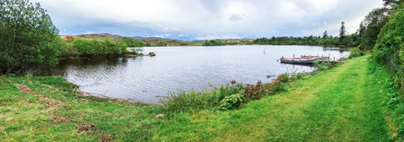 Boats sit at a small dock next to a grassy field surrounding a tiny lake on the island of Islay in Scotland.の写真素材