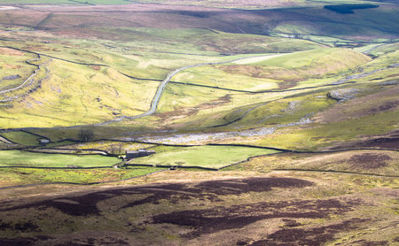 Blotches of shadow from intermittent clouds fall on extensive farmland in the Peak District,...
