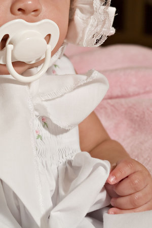 Baby girl dressed in frilly bonnet sucking on a pacifier.