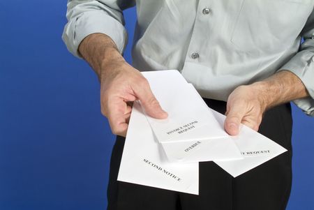 A man holding a several white envelopes with pastdue notices on them. の写真素材