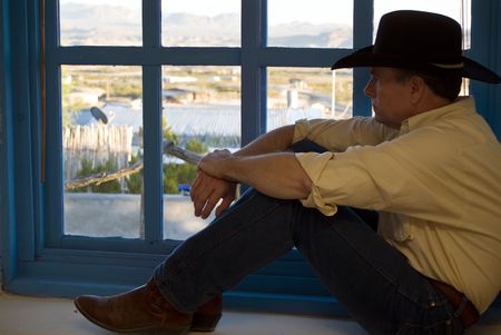 A man dressed in western attire, sitting on the wide windowsill of a colorfully painted window. の写真素材