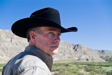 A portrait man in a black western style hat with cliffs and a bright blue sky in the background.の写真素材