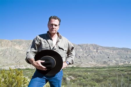 A man standing with his hat in his hand in a gesture of respect for the rugged beauty surrounding him.の写真素材