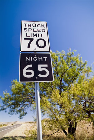 A speed limit sign with bullet holes in it and a scrubby tree and beautiful blue sky as the...