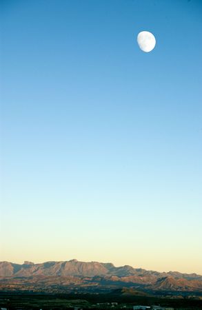 An incredible view of the moon visible over the cliffs of a rock desert during twilight. の写真素材