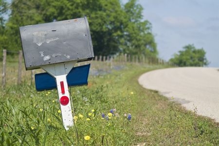 An old peeling mailbox by the side of a wildflower edged country road. の写真素材