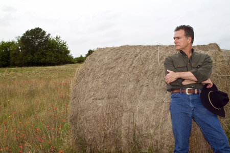 A man resting against a large round bale of hay. の写真素材