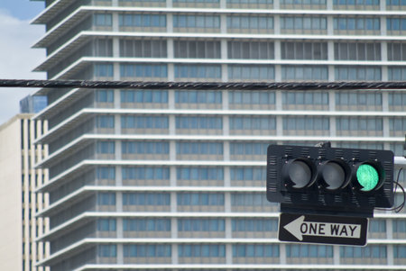 A traffic light on green with one way sign below and out of focus buildig in background. 