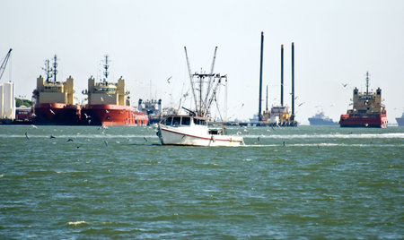 A shrimper navigating his shrimp boat through an industrial harbor. 